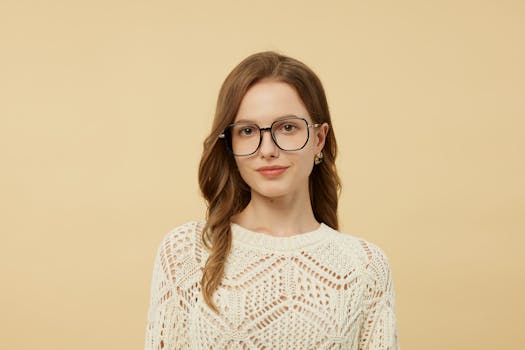 Portrait of a woman in chic glasses and knit sweater against a neutral background.
